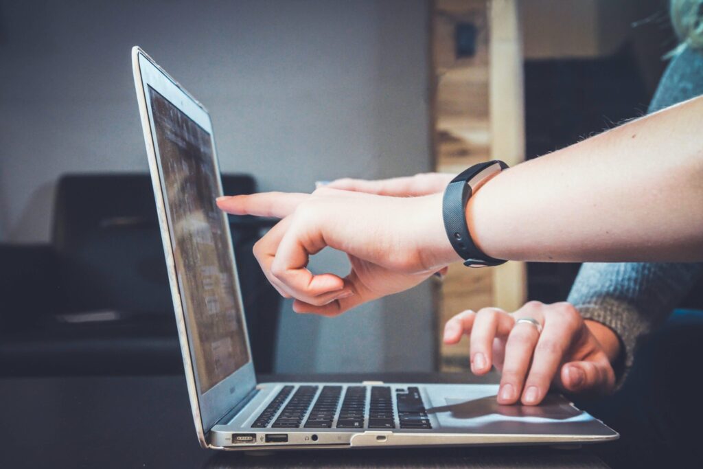 Hands pointing at laptop screen, wearing black wristband, indoor photo.